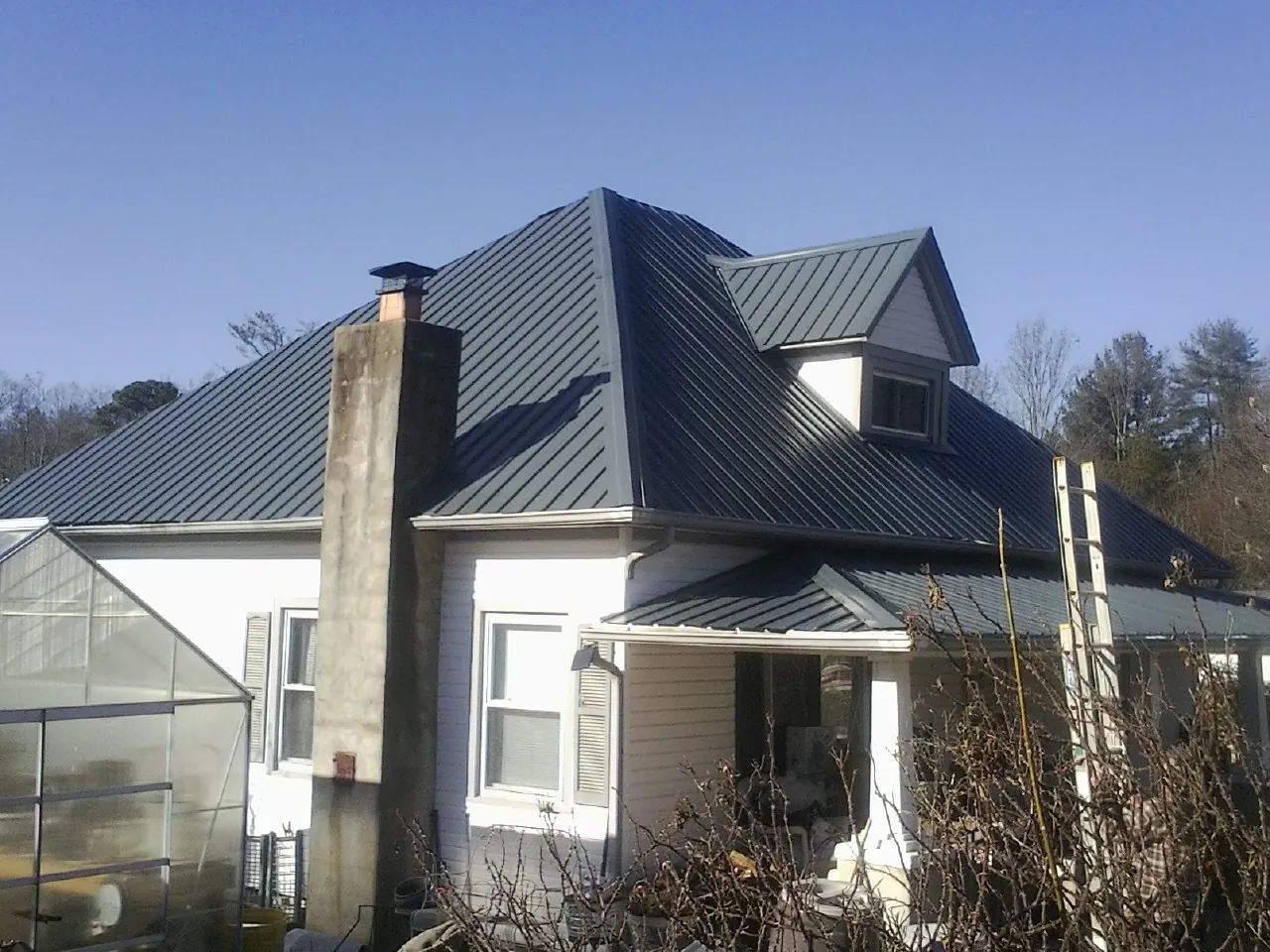 Dark blue standing seam metal roof on a white farmhouse with dormer — Slate & Tile Roof Repair by Roofing Brothers in Slovan