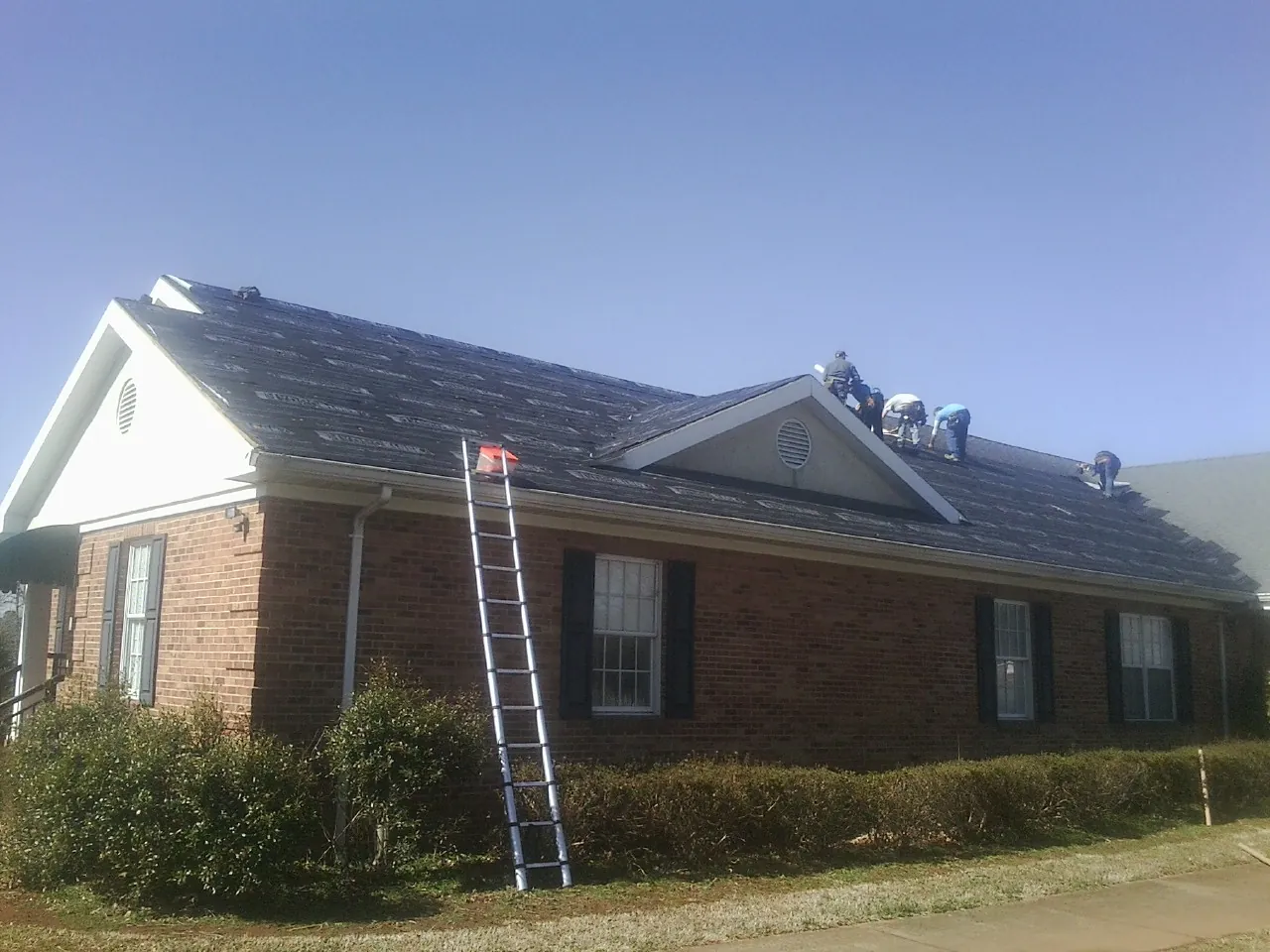 Crew tearing shingles off a brick ranch roof with a ladder set — Emergency Roof Repair work by our crew in Slovan