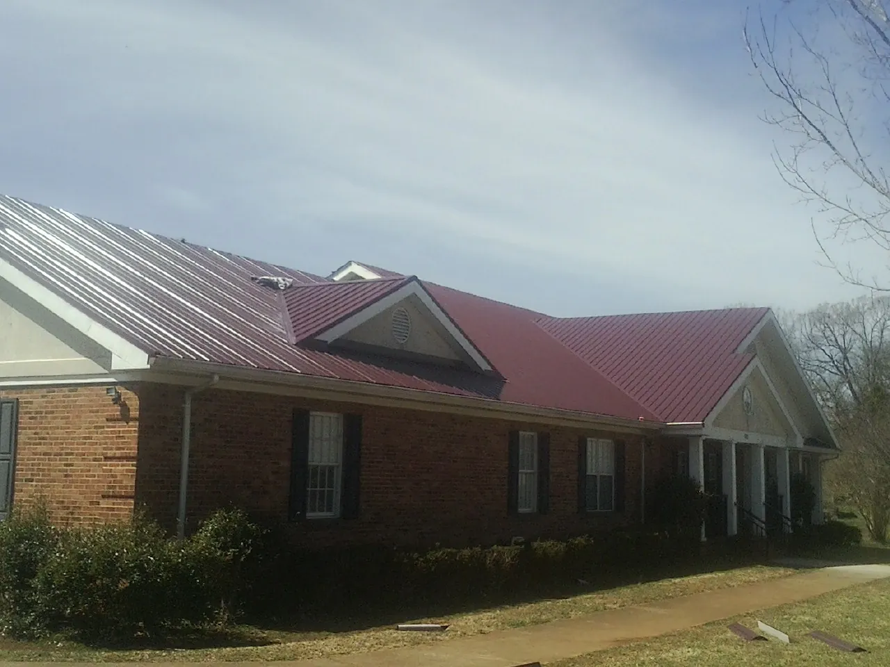 Red metal roof with gabled entries on a long brick building, from a Hail Damage Roof Repair job in Slovan