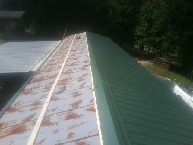 Old rusted panels beside newly installed green metal roofing — Wind Damage Roof Repair by Roofing Brothers in Slovan