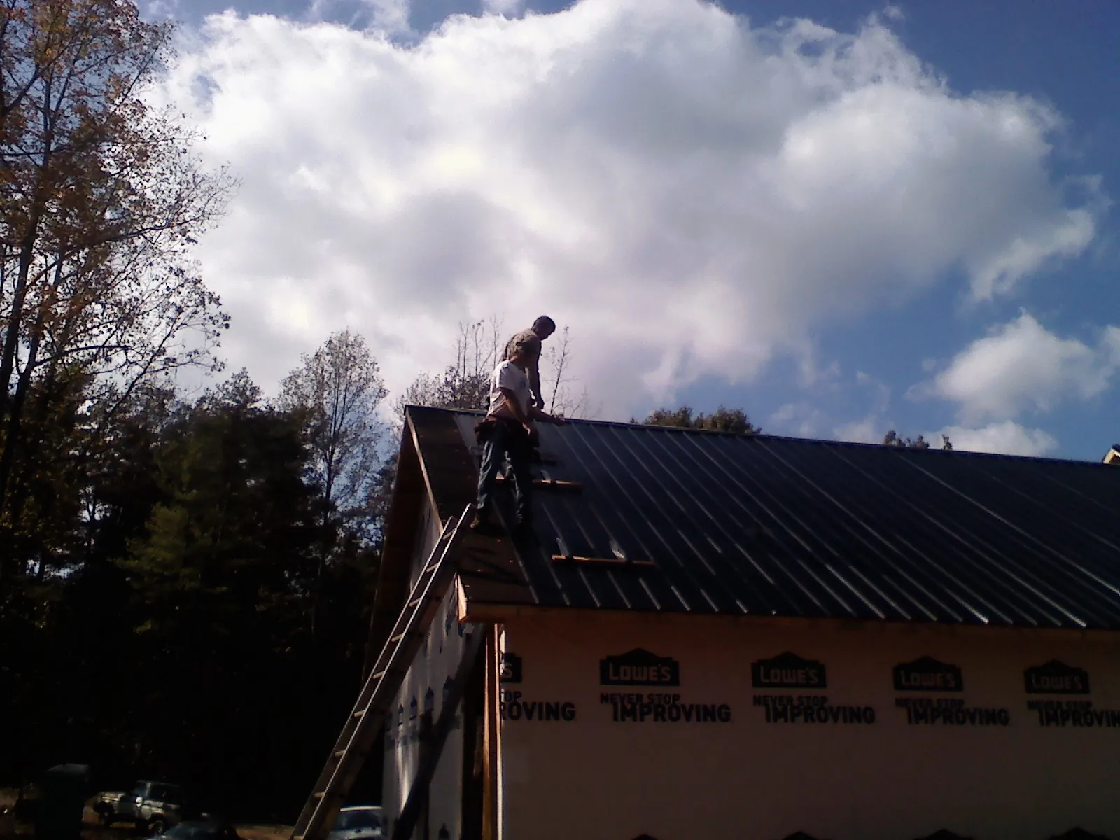 Roofer fastening dark metal panels high against a cloudy sky, from a Roof Inspection job in Slovan